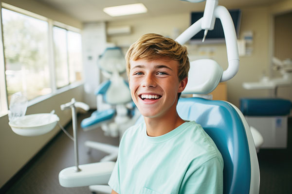 A young man is smiling in a dental office setting, sitting in a dentist s chair with his arms crossed.