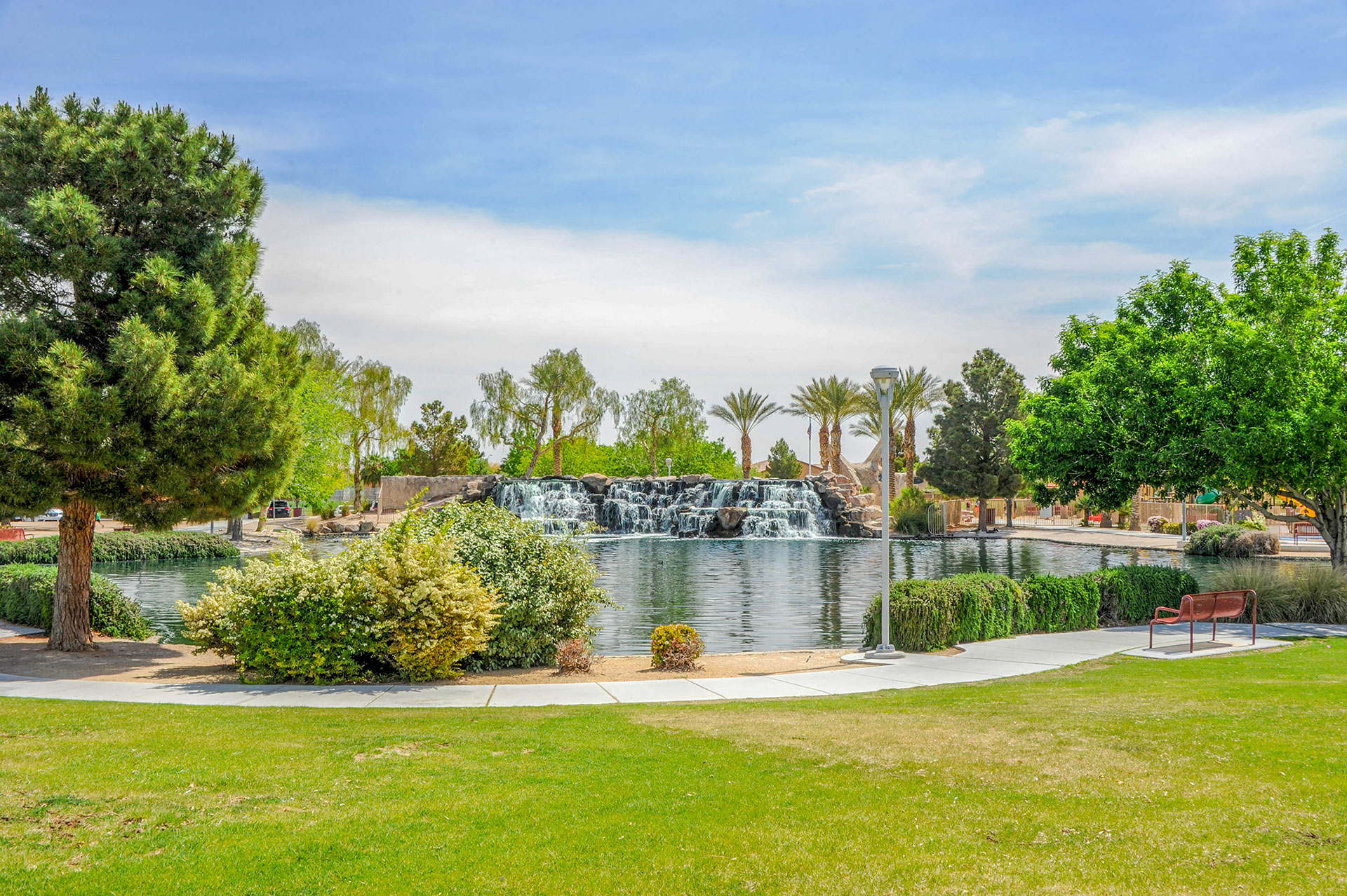 A tranquil park scene with a man-made pond, palm trees, and a fountain in the background.