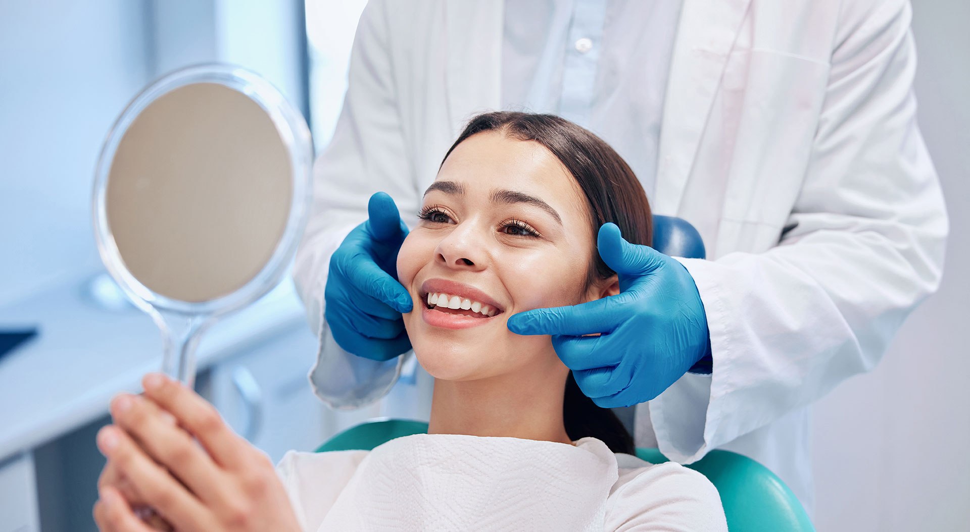 A person is seated in a dental chair, receiving care from a dental professional who stands behind them.