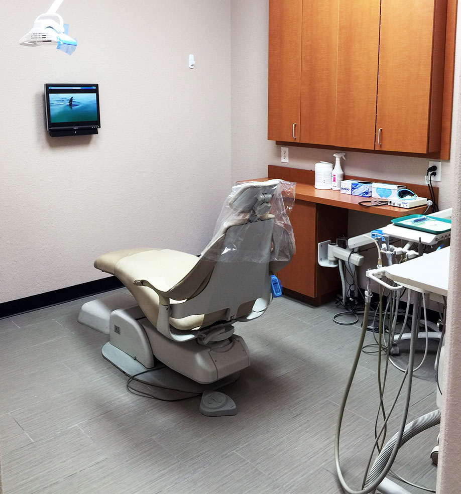 The image shows an interior view of a dental practice with a chair and a desk, featuring a computer monitor displaying what appears to be a patient s dental records or X-rays.