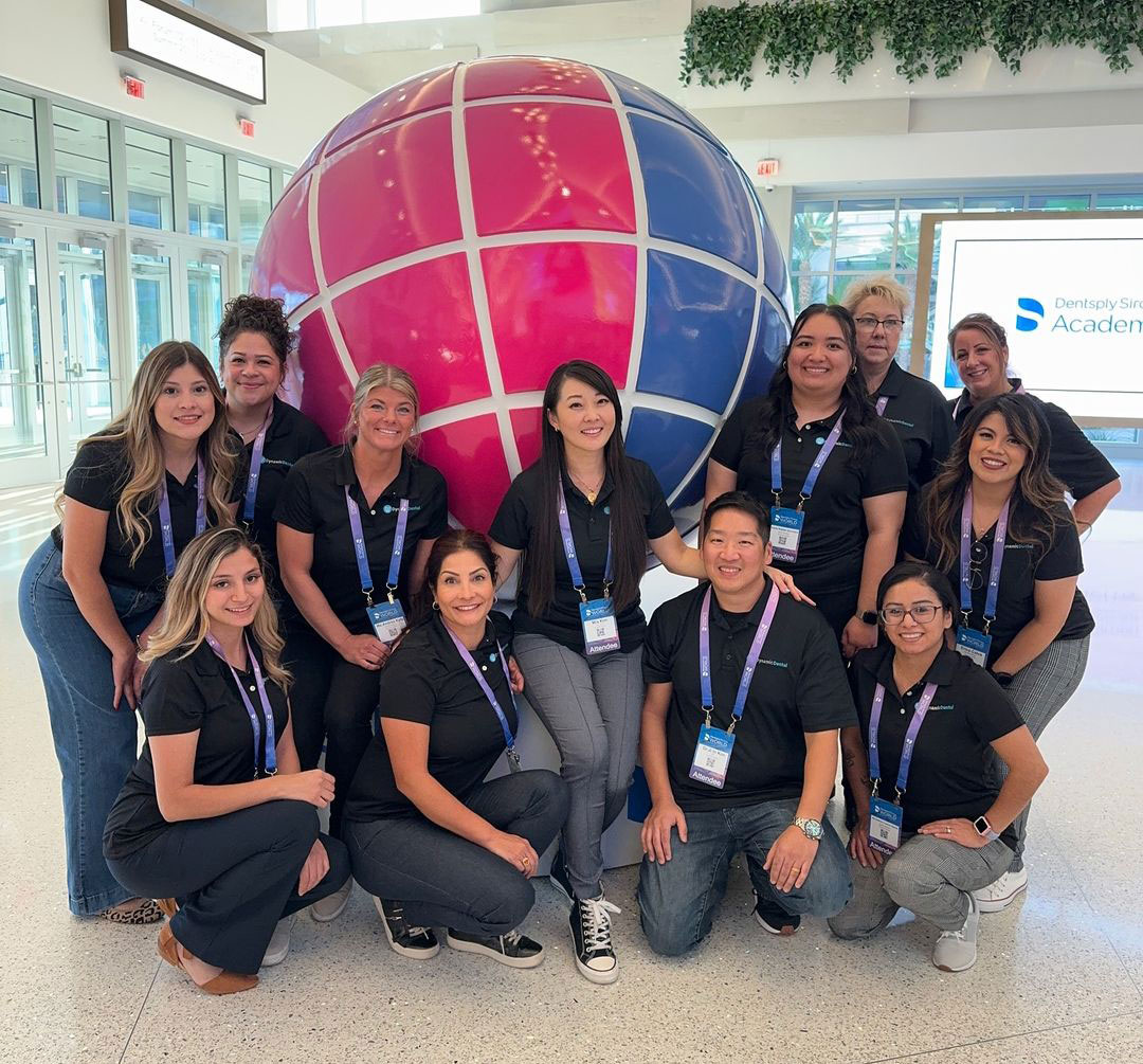 The image shows a group of people posing for a photo with a large, colorful globe in the background. They are standing in front of a sign that reads  SAP  and appear to be at an event or conference.