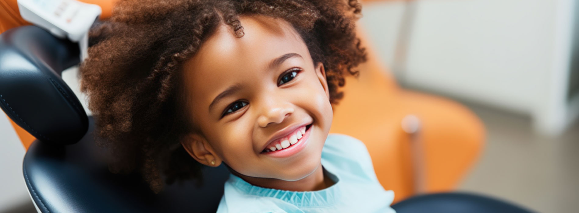 A young child is smiling at the camera while sitting in a dental chair.