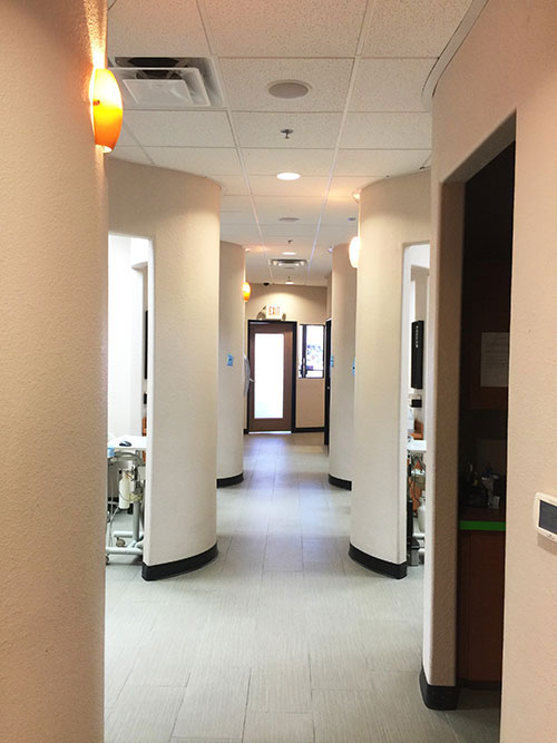 The image depicts an interior hallway with a series of pillars and a long corridor leading to a door at the end.