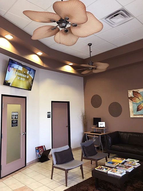 An interior view of a waiting room with a ceiling fan, wall-mounted television, and decorative elements.
